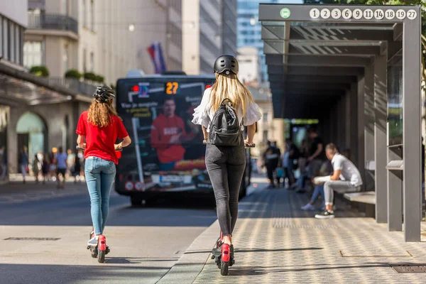 Achteraanzicht van trendy fashinable tienermeisjes paardrijden openbare huur elektrische scooters in stedelijke omgeving. Nieuw milieuvriendelijk modern openbaar vervoer in Ljubljana, Slovenië — Stockfoto