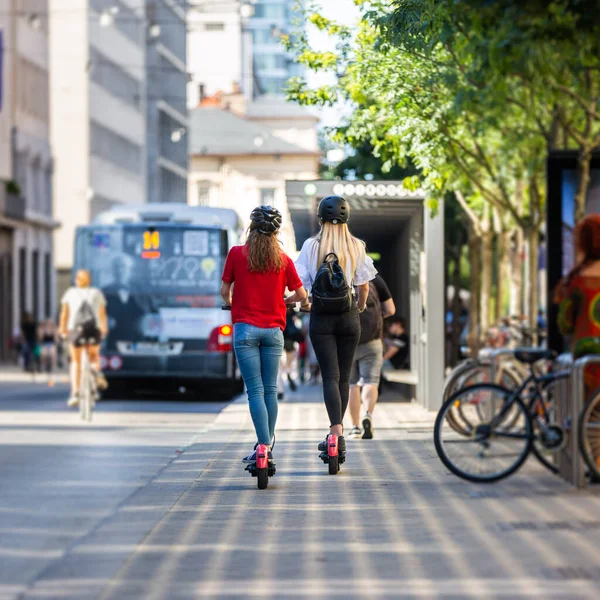 Vue arrière des adolescentes à la mode fashinable équitation scooters électriques de location publique dans l'environnement urbain de la ville. Nouveau transport urbain moderne et écologique à Ljubljana, Slovénie — Photo