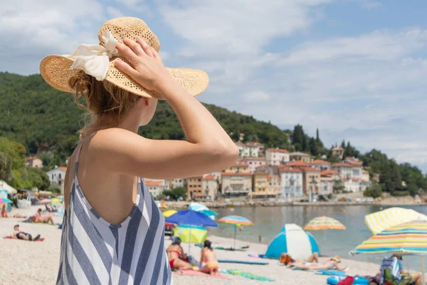 Dama con vestido de verano a rayas y sombrero de paja relajándose en la vacción disfrutando de la vista sobre la playa en Moscenicka Draga, Istria, Croacia —  Fotos de Stock