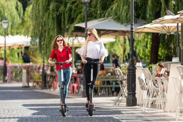 Странные девочки-подростки, катающиеся на арендованных электрических скутерах в городской среде. Новый экологически чистый современный городской транспорт в Любляне, Словения — стоковое фото