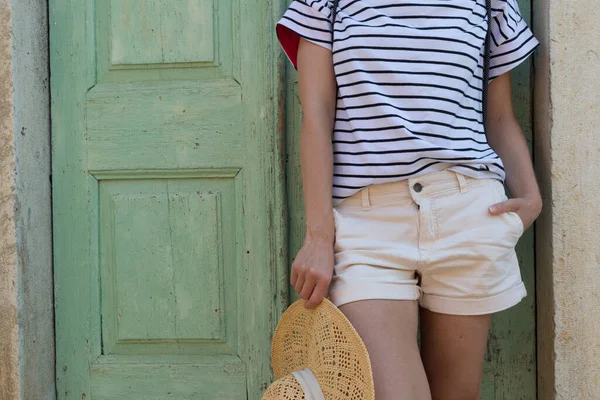 Модный портрет женщины в солнцезащитной шляпе, стоящей и расслабляющейся в тени перед бирюзовой деревянной дверью винатажа в старом средиземноморском городе во время наблюдения за жарким летним днем — стоковое фото