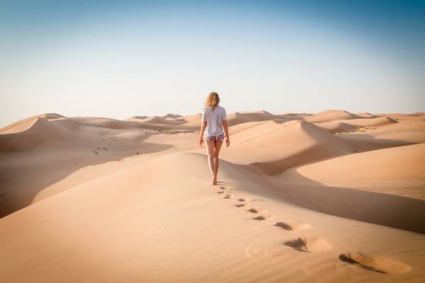 Blonde female Caucasian traveler leaving footprints in sand dunes when walking in dessert in Oman — Stock Photo, Image