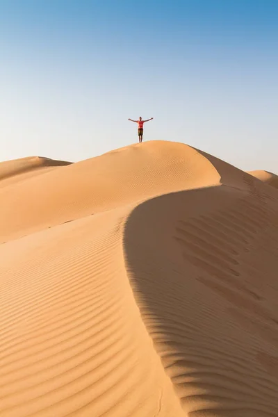 Mannelijke reiziger staat op de top van duin, armen omhoog naar de hemel, tijdens het reizen zand dessert in Oman. — Stockfoto