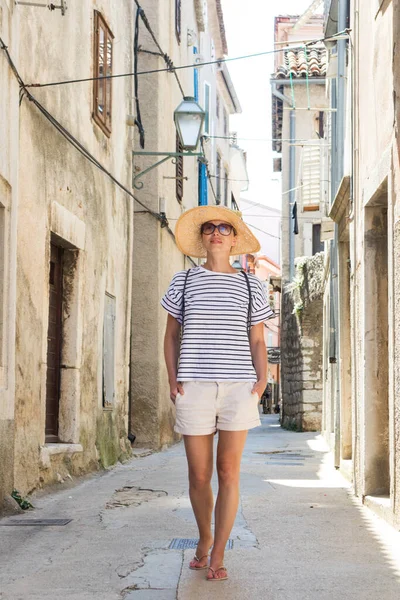 Linda loira jovem viajante do sexo feminino vestindo chapéu de sol de palha passear e desfrutar de férias de verão em uma antiga cidade costeira tradicional ao custo Adriático, Croácia — Fotografia de Stock