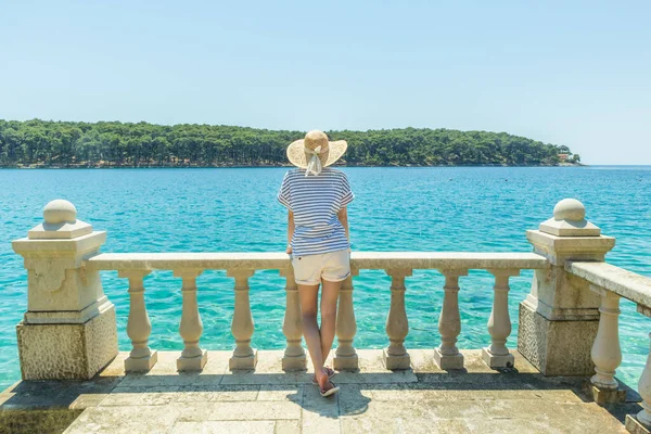 Bakifrån av kvinna bär halm sommar hatt, lutar sig mot eleganta gamla sten staket av kustnära villa, koppla av medan du tittar på blå Adriatiska havet, på ön Losinj Kroatien. — Stockfoto