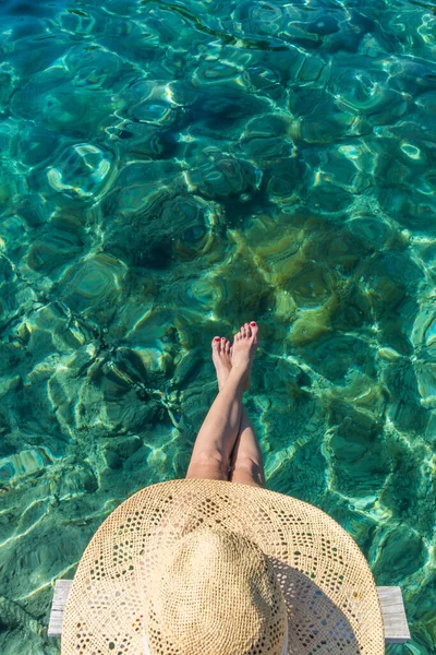 图上的自上而下的女性头像，戴着大大的夏日太阳帽，在碧绿的大海中悠闲自在地躺在木制小码头上 — 图库照片