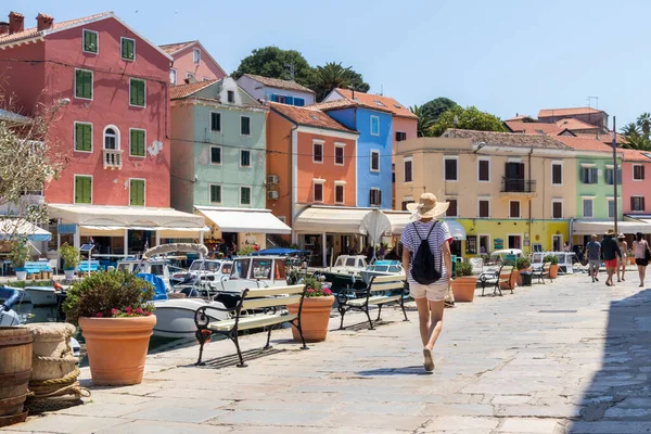 Visão traseira da bela loira jovem viajante vestindo chapéu de sol palha passear e desfrutar de férias de verão em uma antiga cidade costeira tradicional de Veli Losinj, Adriático custo, Croácia — Fotografia de Stock