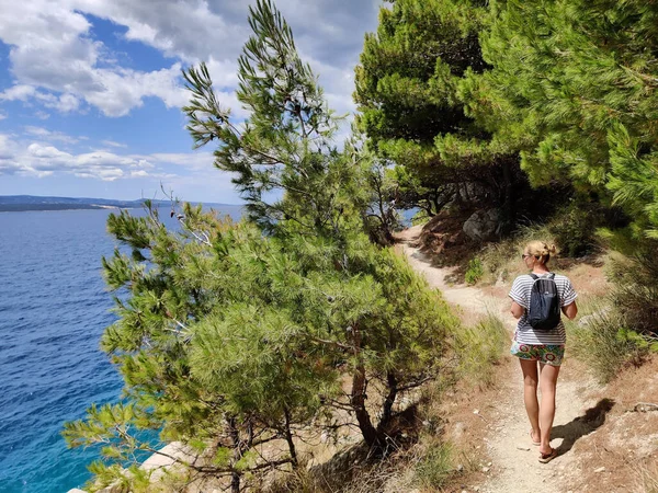 Jonge actieve feamle toerist draagt kleine rugzak lopen op het kustpad tussen pijnbomen op zoek naar afgelegen inham om alleen te zwemmen in vrede aan zee in Kroatië. Reis- en avontuurconcept — Stockfoto