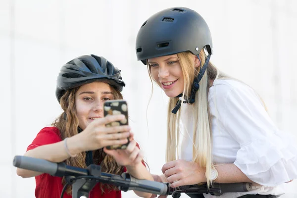 Adolescentes meninas usando aplicativo móvel para desbloquear e alugar passeios de aluguel público scooters elétricos em ambiente urbano da cidade. Transporte público moderno e ecológico em Ljubljana, Eslovénia — Fotografia de Stock