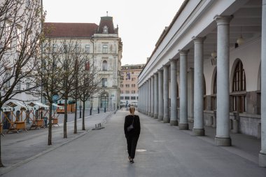 Corona virüsü salgını sırasında orta çağ Ljubljana şehir merkezinde yürüyen tanınmayan bir kadının arka görüntüsü. Sokaklarda neredeyse hiç insan yok.