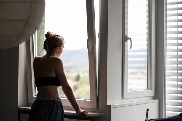 Home quarantine and social distancing during covid pandemic. Silhouette of lonley caucasian woman standing by window, anxiously looking out. Coronavirus infection, pandemics, disease outbreaks