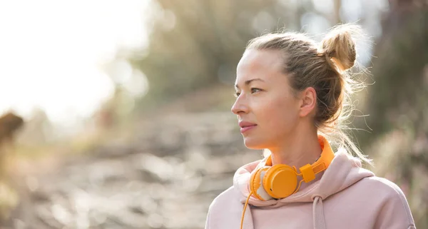 Porträt der schönen Sportlerin mit Kapuzenpulli und Kopfhörer beim Training im Freien. — Stockfoto