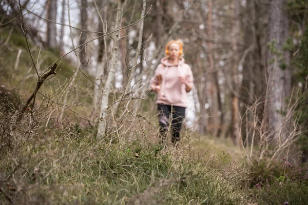 Aktiv sportig kvinna lyssnar på musiken när hon springer i höstskogen. Kvinnliga löpare utbildning utomhus. Friska livsstil bild av unga kaukasiska kvinna jogga utanför — Stockfoto