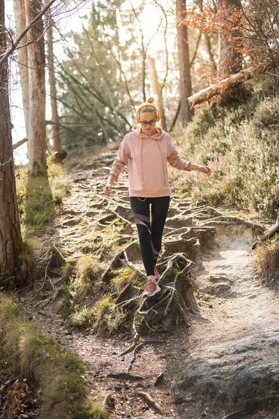 Actieve sportieve vrouw rent in de herfst herfst bos springen over de wortels op het pad. Gezond levensstijl imago van jonge actieve blanke vrouw joggen buiten in de natuur — Stockfoto