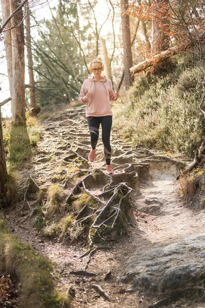 Actieve sportieve vrouw die naar de muziek luistert terwijl ze in het herfstbos rent. Vrouwelijke loper training buiten. Gezond levensstijl imago van jonge blanke vrouw joggen buiten — Stockfoto