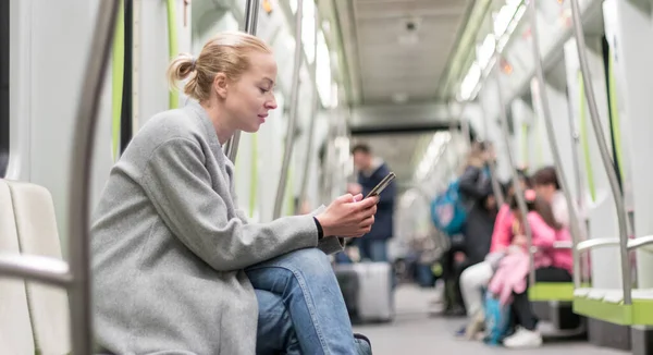 Portret uroczej dziewczyny wpisującej wiadomość na telefonie komórkowym w prawie pustym publicznym pociągu metra. Pozostawanie w domu i dystansowanie społeczne zalecane z powodu wybuchu pandemii wirusa korony — Zdjęcie stockowe