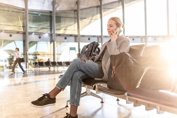 Jovem loira casual usando seu telefone celular enquanto espera para embarcar em um avião nos portões de partida do aeroporto. — Fotografia de Stock