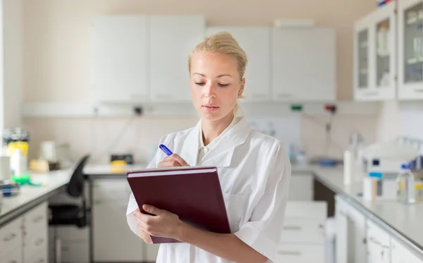 Portrait of young, confident female health care professional taking notes during inventory in scientific laboratory or medical doctors office — Stock Photo, Image