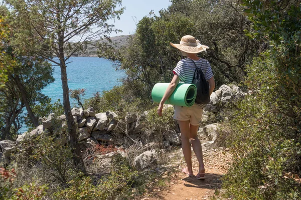 Fiatal aktív feamle turista visel kis hátizsák sétál a tengerparti ösvényen fenyőfák között keresi a távoli öböl úszni egyedül békében a tengerparton Horvátországban. Utazási és kalandkoncepció — Stock Fotó