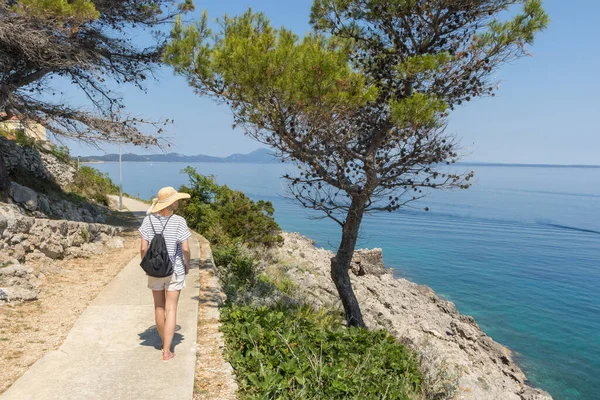 Joven turista activo con una pequeña mochila caminando por el sendero costero entre pinos que buscan una cala remota para nadar solo en paz en la costa de Croacia. Concepto de viaje y aventura — Foto de Stock