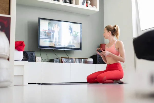 Atrakcyjna sportowa kobieta ćwicząca w domu, ćwicząca pilates przed telewizorem w swoim małym mieszkaniu. Oddalenie się od społeczeństwa. Bądź zdrowy i pozostań w domu podczas pandemii wirusa korony — Zdjęcie stockowe