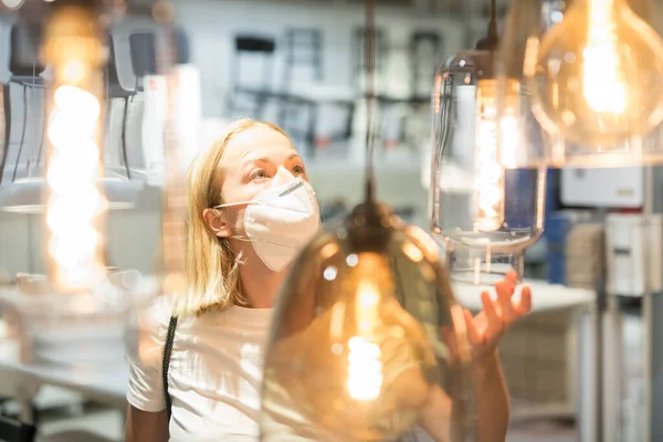 Nueva normalidad durante la epidemia de covidio. Mujer caucásica comprando en la tienda de muebles y accesorios para el hogar usando mascarilla médica protectora para evitar la propagación del virus corona — Foto de Stock