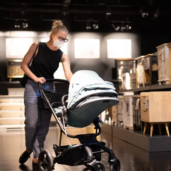 Bebek arabasında yeni doğmuş bir anne, Corona virüsünün yayılmasını önlemek için perakende mobilya ve aksesuar mağazasında koruyucu maske takıyor. Çovid salgını sırasında yeni normal — Stok fotoğraf