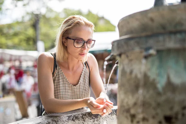 Žíznivý mladý ležérní okurka žena pitná voda z veřejného města fontána v horkém letním dni — Stock fotografie