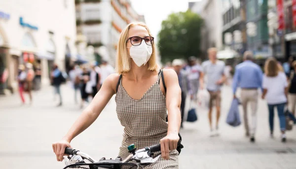 Женщина на велосипеде на городской улице носит медицинскую маску на людях, чтобы предотвратить распространение коронного вируса. Новая норма во время эпидемии ковидов. — стоковое фото