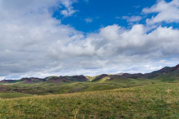 Kırmızımsı tepeler, bulutlu bir günde ilk bahar çimen ile kaplı. Çevresi Arkharly Pass, Kazakistan
