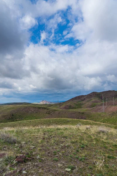 Kırmızımsı tepeler, bulutlu bir günde ilk bahar çimen ile kaplı. Çevresi Arkharly Pass, Kazakistan