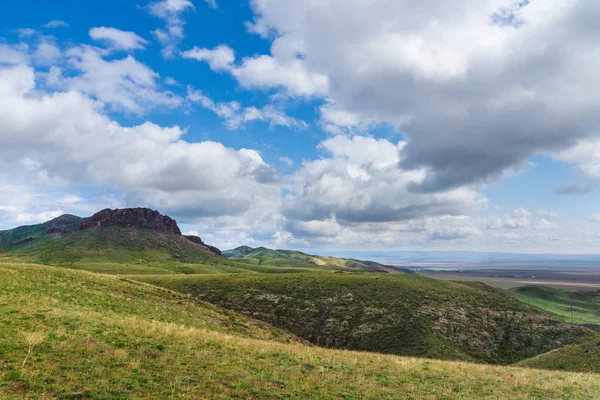 Kırmızımsı tepeler, bulutlu bir günde ilk bahar çimen ile kaplı. Çevresi Arkharly Pass, Kazakistan