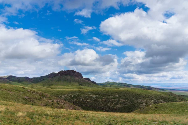 Kırmızımsı tepeler, bulutlu bir günde ilk bahar çimen ile kaplı. Çevresi Arkharly Pass, Kazakistan