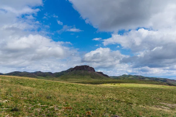 Kırmızımsı tepeler, bulutlu bir günde ilk bahar çimen ile kaplı. Çevresi Arkharly Pass, Kazakistan