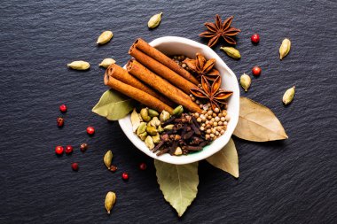 Egzotik bitkisel gıda kavramı organik baharat tarçın sopa, kakule bakla, defne yaprağı, yıldız anason ve kişniş seedsin beyaz seramik kupa kopya ile siyah arduvaz taş plaka üzerinde karışımı