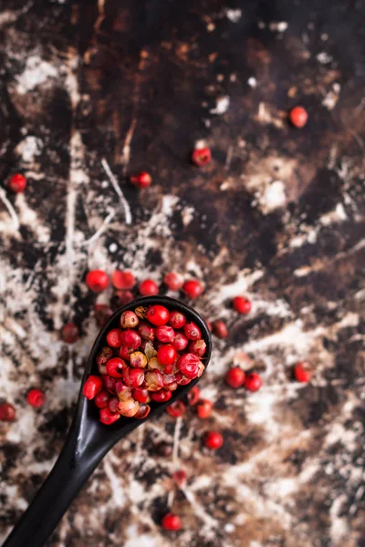 Close up Organic pink peppercorns or pink berry in black ceramic spoon on rustic metal blackground