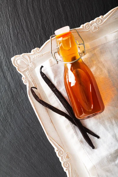 Homemade vanilla extract in glass bottle and vanilla beans on black background with copy space