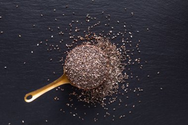 Yiyecek baharatları konsepti. Bakır bardaktaki organik chia tohumunun fotokopi alanı ile siyah taş üzerinde üst görünümü.