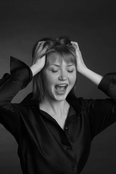 black and white Studio portrait of a young woman with short hair in a black blouse. she screams, holding her head in her hands. The concept of hysteria and depression