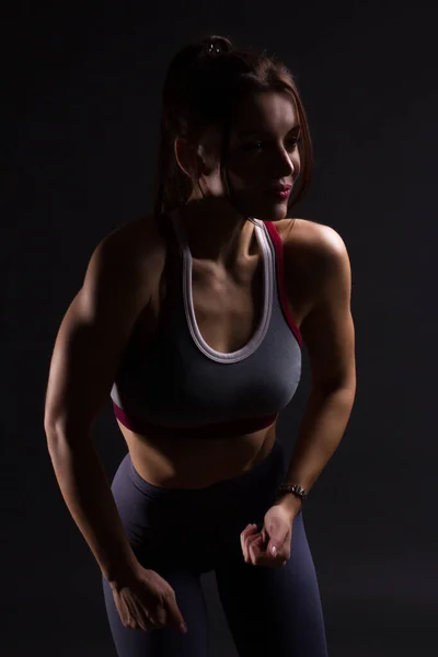 Fitness young woman in training clothes, dark colors backlit photo