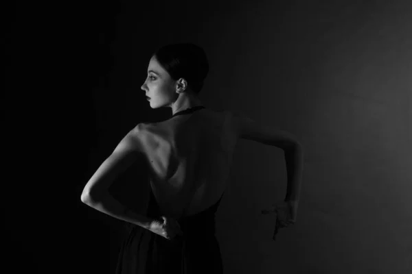 monochrome vintage dramatic portrait of a girl in the Studio on gray background. view from the back, a ballerina dancing and gesticulating