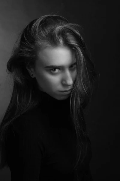 A young woman with disheveled hair. Black-and-white dramatic portrait. Looks from under his brows