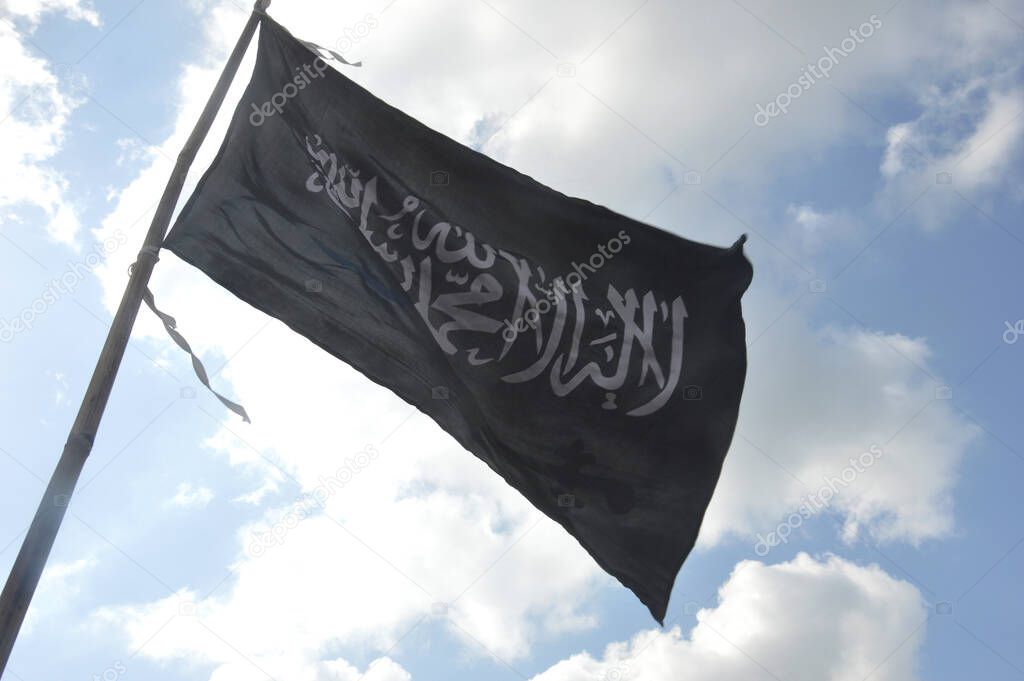 Black tauhid flag aginst blue sky and white clouds