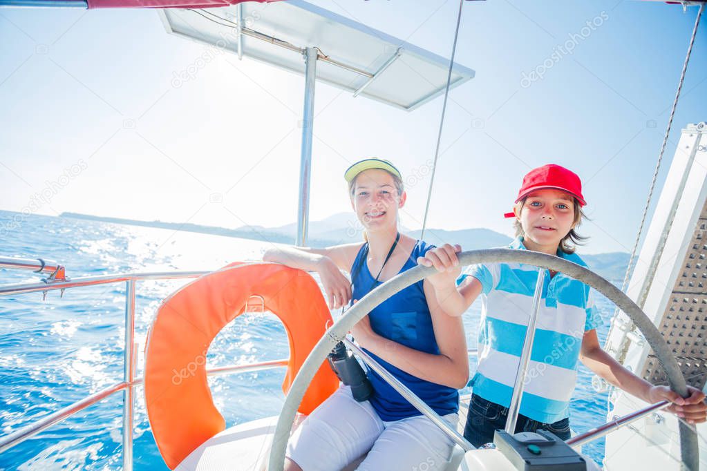 Boy captain with his sister on board of sailing yacht on summer cruise. Travel adventure, yachting with child on family vacation.