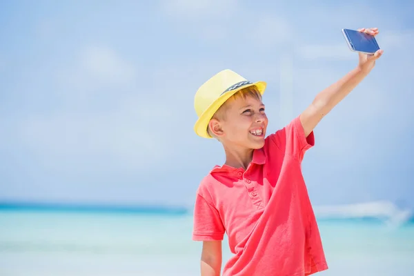 Glückliches Kind mit gelbem Hut, das Selfie macht und Spaß am tropischen Strand hat. Sommerferienkonzept — Stockfoto