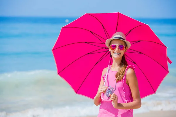 Menina com um guarda-chuva rosa na praia de areia — Fotografia de Stock