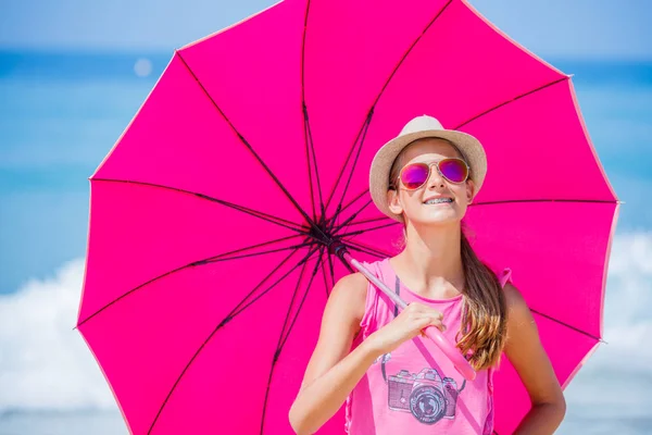 Menina com um guarda-chuva rosa na praia de areia — Fotografia de Stock