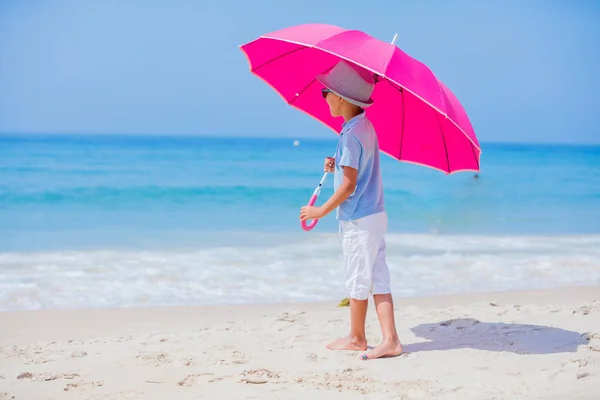 Niño con un paraguas rosa en la playa de arena —  Fotos de Stock