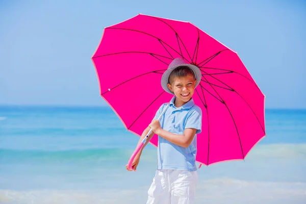 Menino com um guarda-chuva rosa na praia de areia — Fotografia de Stock