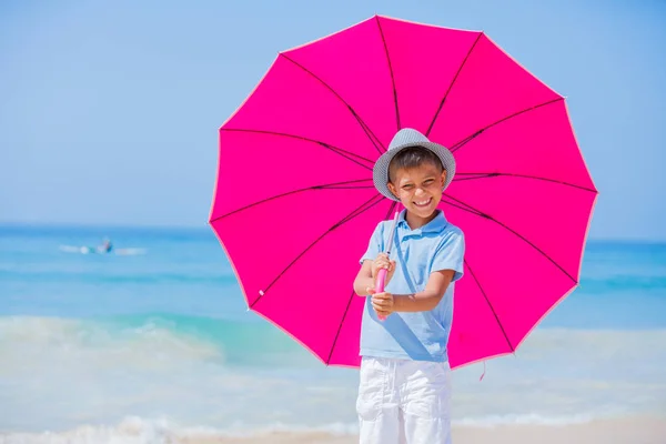Хлопчик з рожевою парасолькою на піщаному пляжі — стокове фото